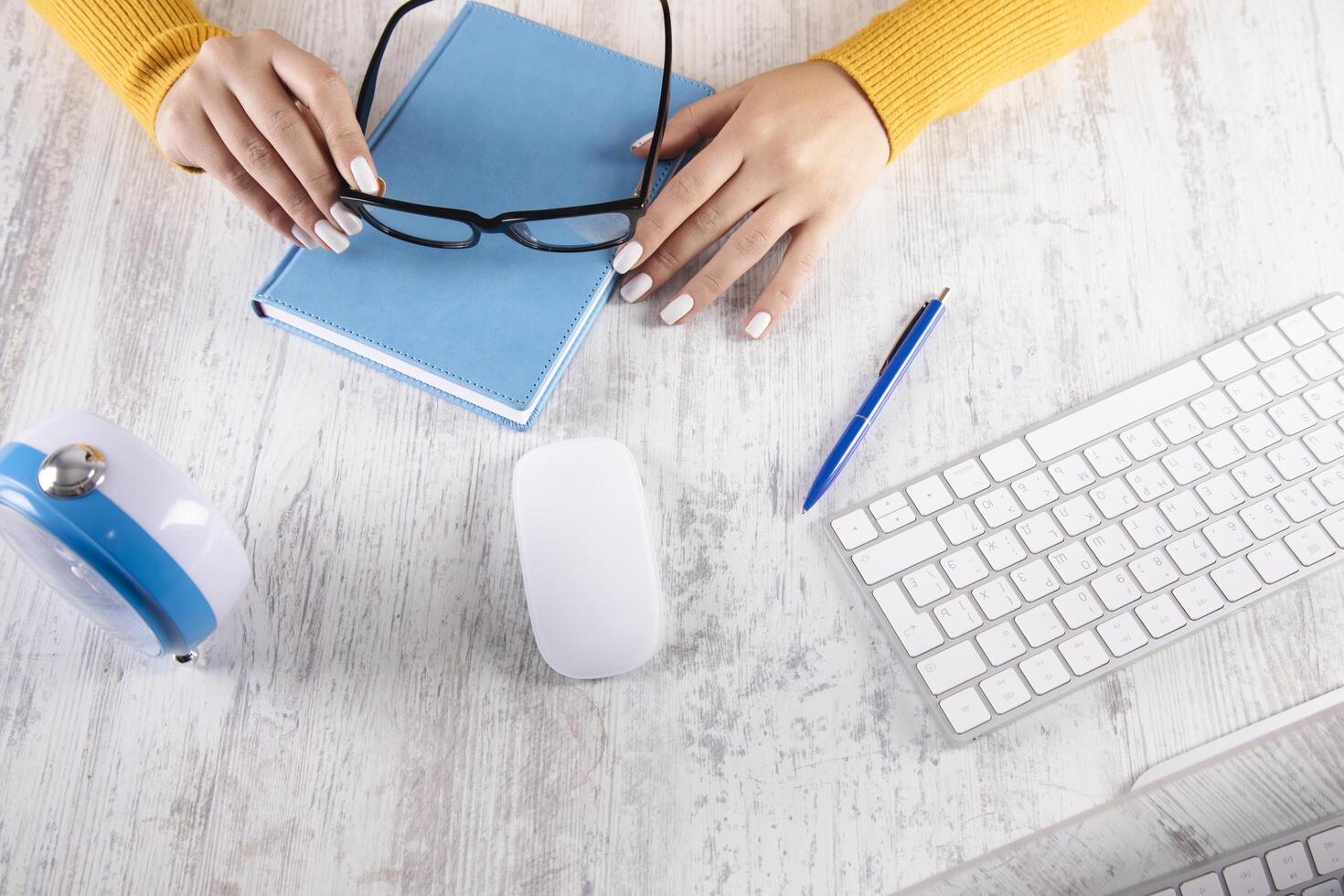 A woman's hands are on a desk with a computer, mouse and glasses photo