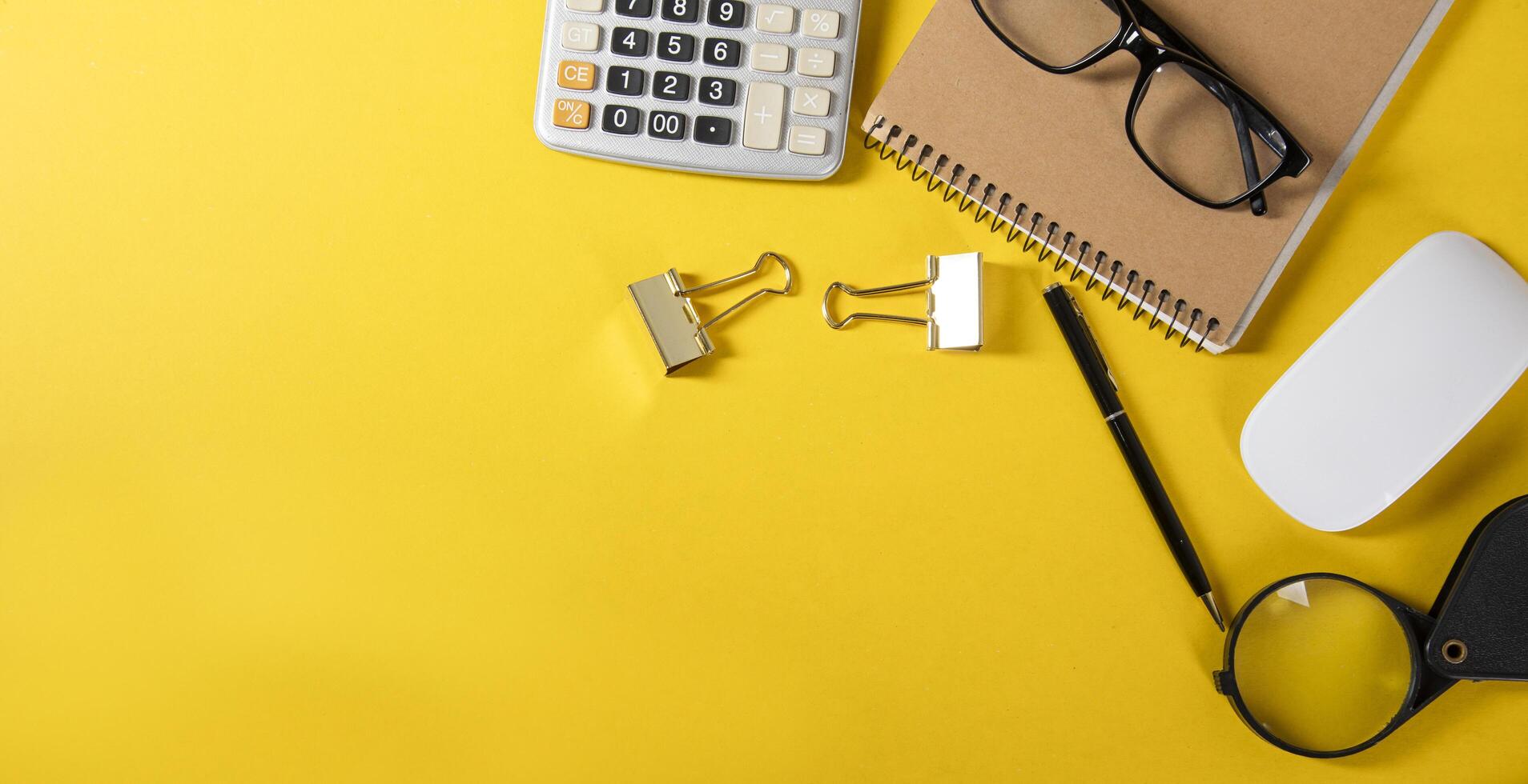 A yellow background with a calculator, glasses, and a pen photo