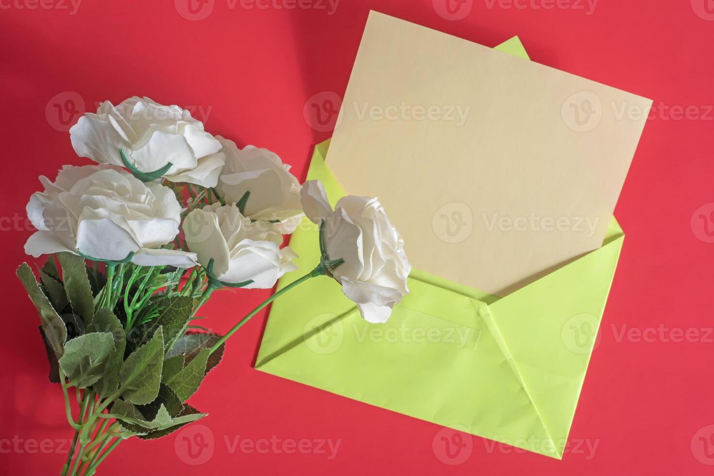 An envelope with white roses and a green envelope on a red background photo