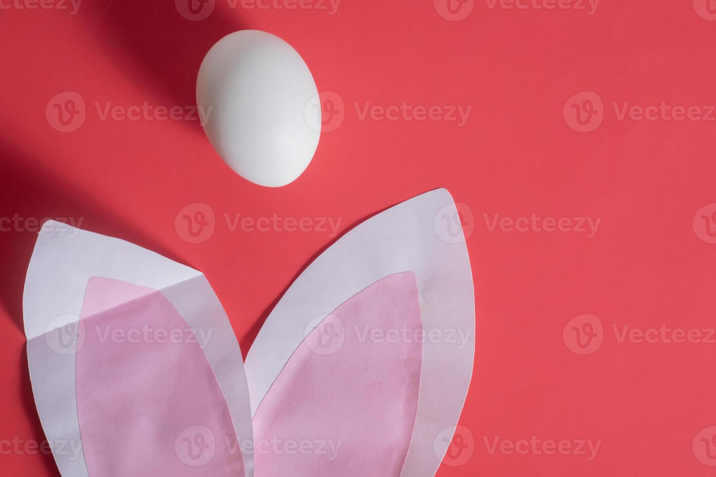 A white egg and a pink paper rabbit on a red background photo