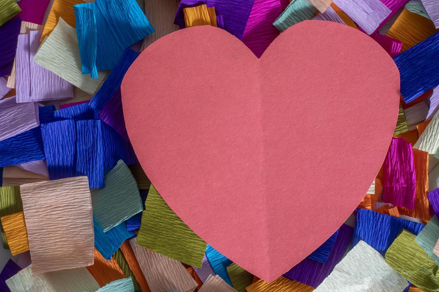 Red heart on a multi-colored paper background symbolizing the celebration of love photo