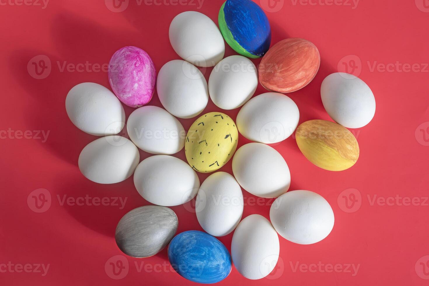 Decorative colorful eggs amidst white eggs on a vibrant red background, top view photo