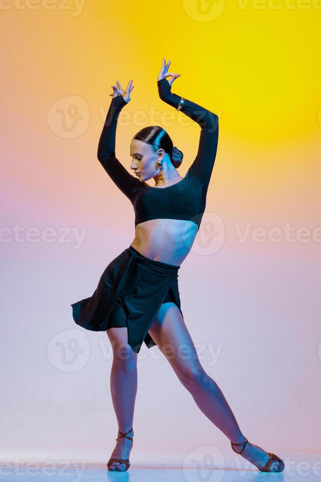 Stylish female dancer in black outfit posing in Latin dance move on vibrant gradient studio background photo