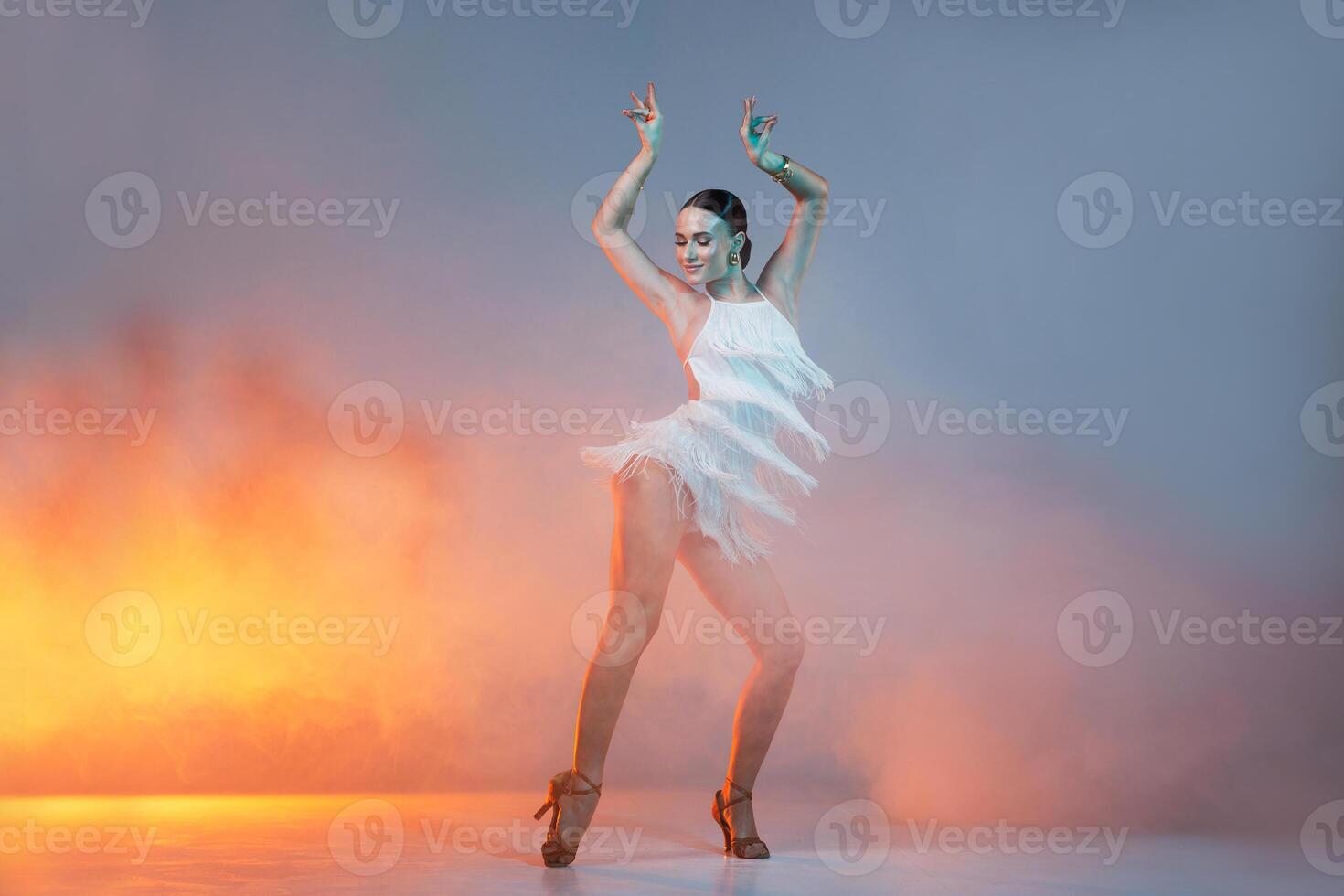 Elegant female Latin dancer in a white fringed dress performing a dynamic move with grace and confidence in artistic lighting photo