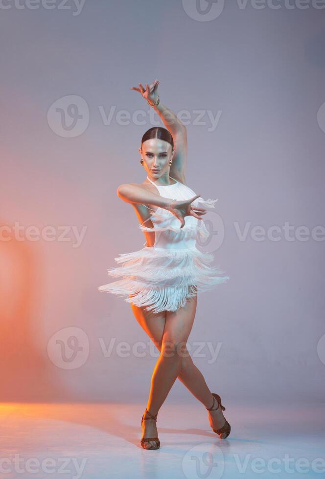Elegant female Latin dancer in a white fringed dress performing a dynamic move with grace and confidence in artistic lighting,,, photo