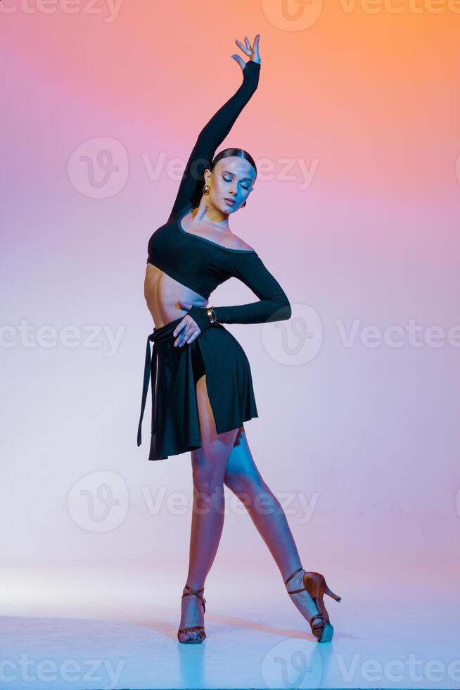 Stylish female dancer in black outfit posing in Latin dance move on vibrant gradient studio background.. photo