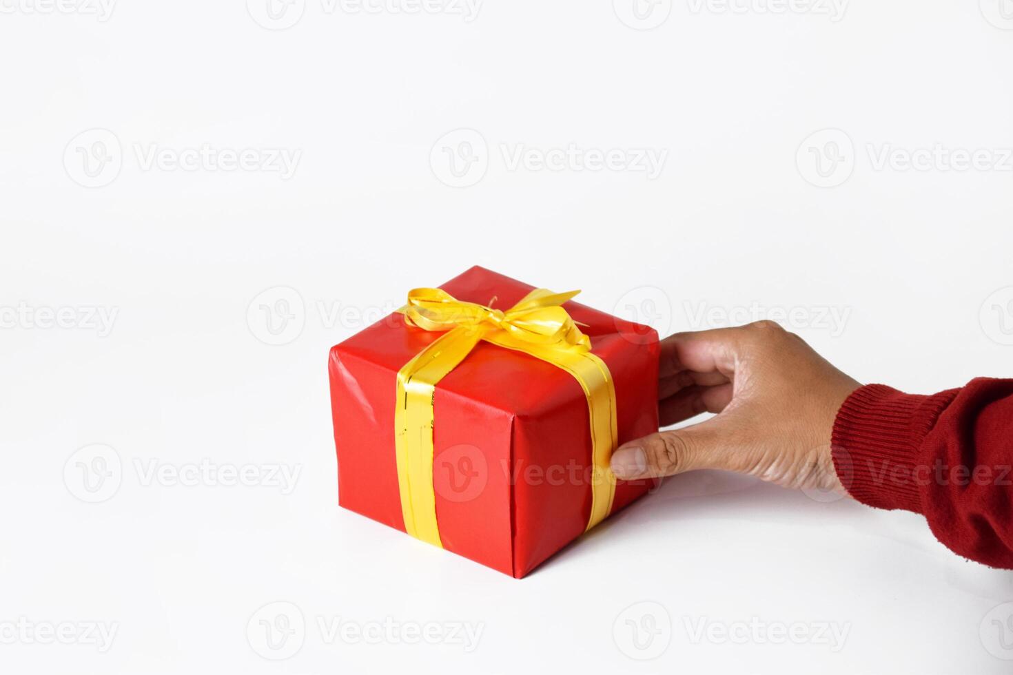 The hand of a person wearing a red sweater holds and shows a red gift box photo