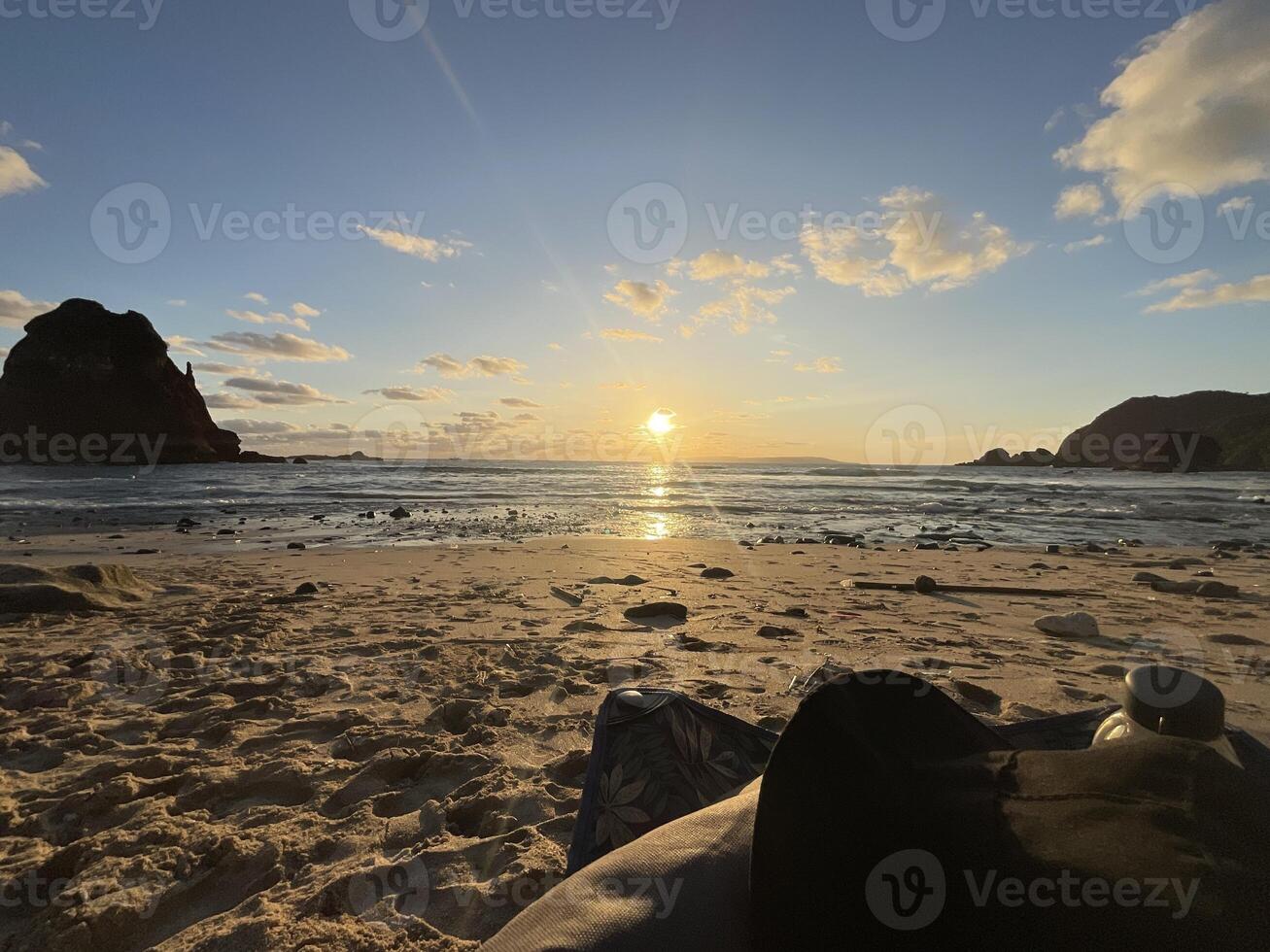 Sunset view of Papuma Beach in Jember, featuring a rocky islet standing tall against the warm hues of the setting sun. The sky transitions from deep blue to orange. Papuma Beach Jember, Indonesia photo