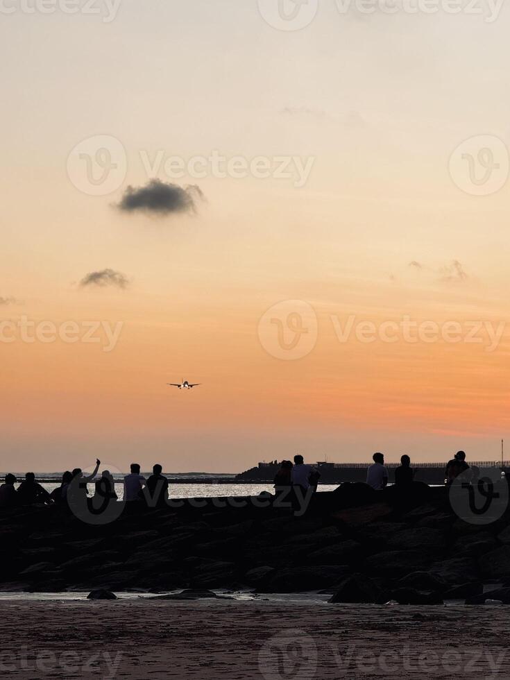 Sunset at Kelan Beach Bali with Airplane Landing and Silhouettes of People Enjoying the Scenic View. Golden Hour Sky, Tranquil Atmosphere, Tropical Destination, Travel, Tourism, Coastal Photography photo