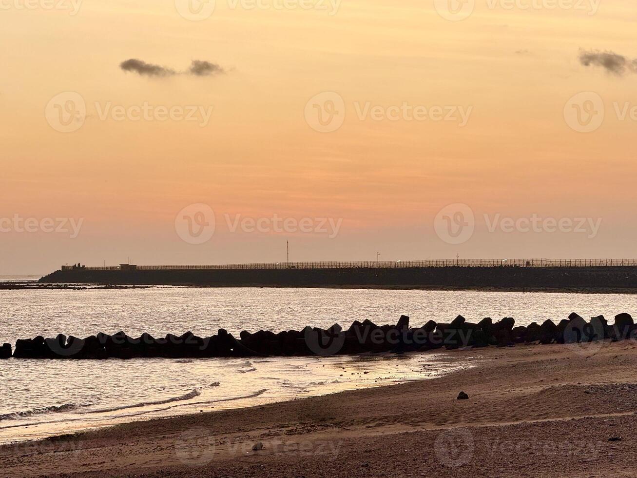 sunset over Kelan Beach, Bali, with calm ocean waves and a scenic breakwater. A tranquil coastal scene with warm hues and serene atmosphere. photo