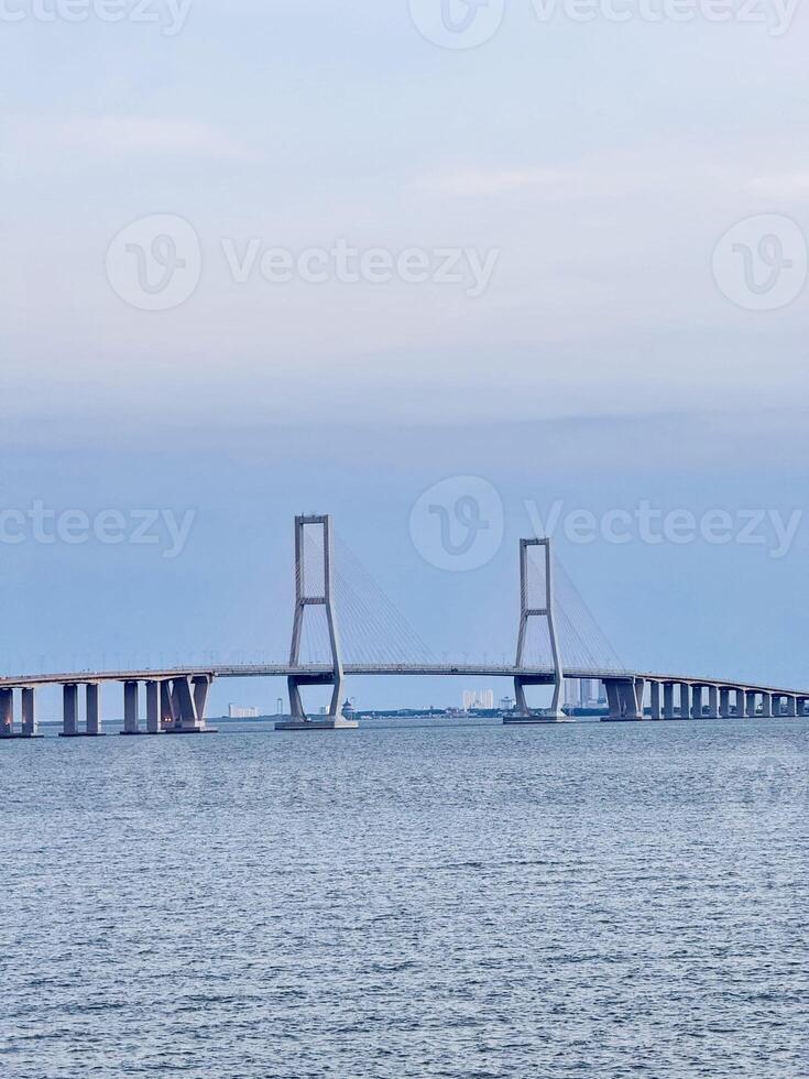 Suramadu Bridge Over Madura Strait with Calm Ocean and Blue Sky Longest Cable-Stayed Bridge in Indonesia, Coastal View, Urban Skyline, Maritime Landmark, Travel Destination, Tourism, Architecture. photo
