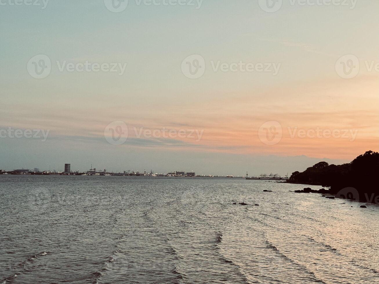 Golden Sunset view and Suramadu Bridge, View from Surabaya to Madura with Harbor and Silhouettes of Ships on the Horizon. A Scenic Twilight Over the Ocean, Dramatic Clouds, Vibrant Sky photo
