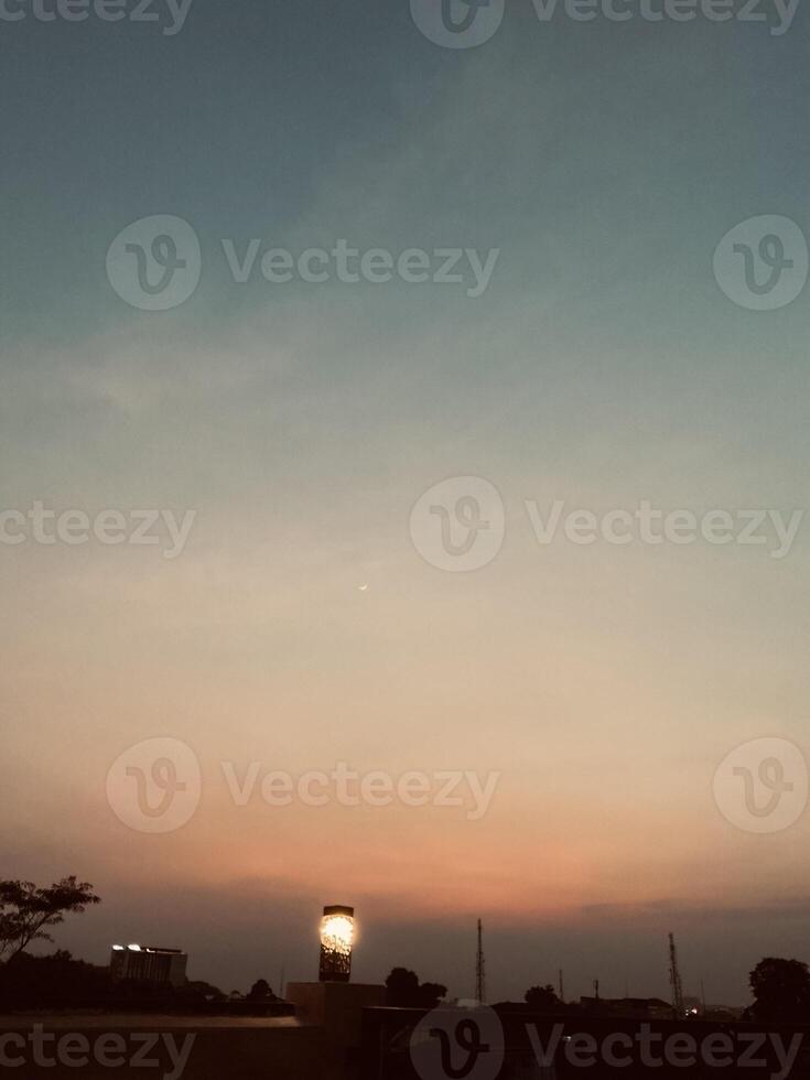 A cozy cafe corner with a vintage lamp casting soft glow as twilight paints the sky in warm orange, pale blue. Distant towers silhouette against dusky sky, adding a tranquil depth. photo