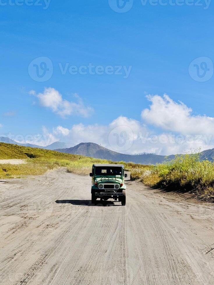 Off-Road Vehicle on Dirt Road with Mountain and Cloudy Sky View. Bromo National Park. photo