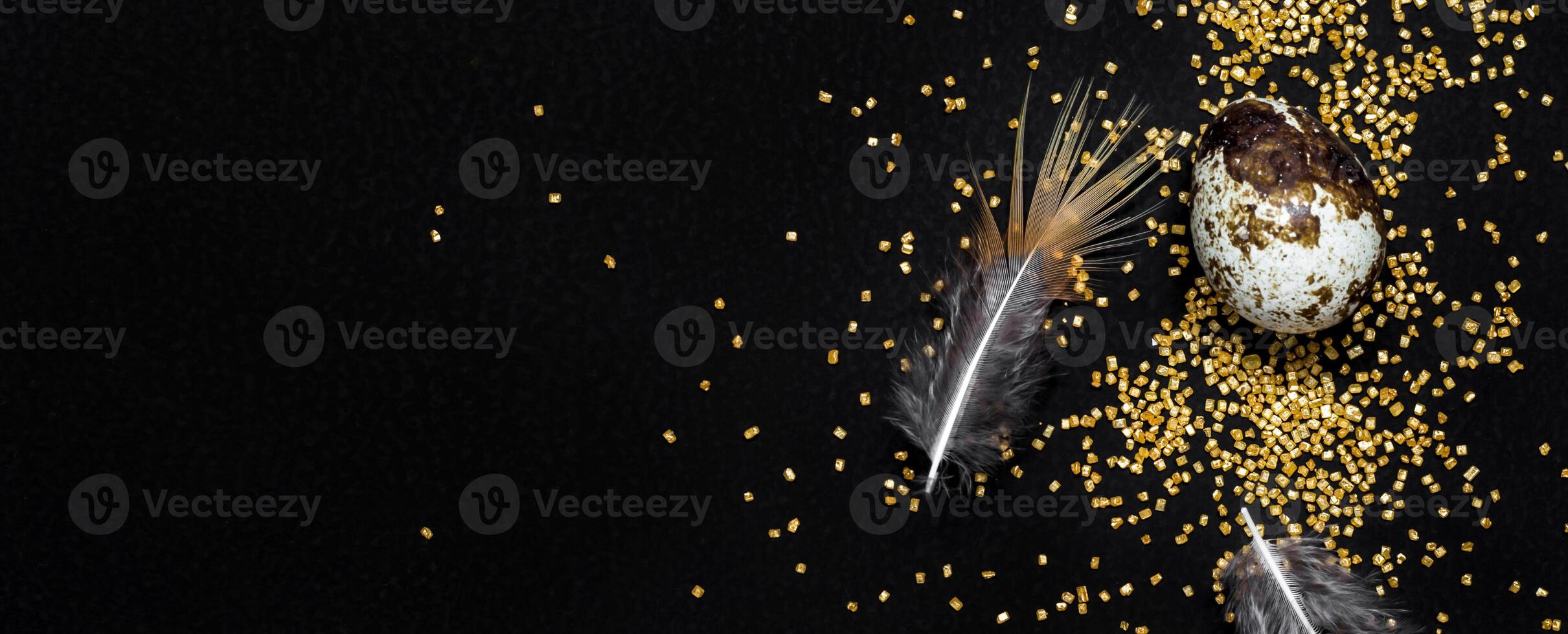 Quail eggs, feathers and golden sugar sprinkles on black. Moody easter background, banner format photo
