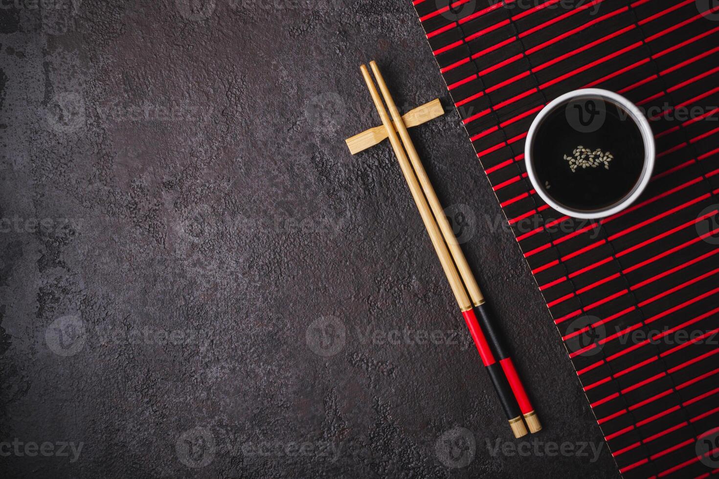 Bamboo chopsticks, soy sauce bowl and striped mat on black background. Asian Japanese table setting photo