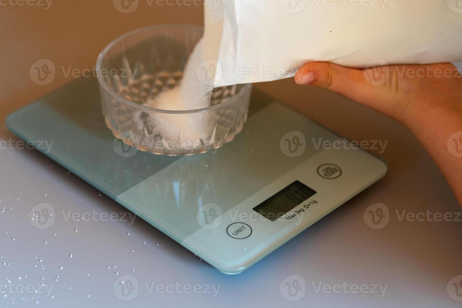 Weighing sugar from a pack on a kitchen scale on the kitchen table photo
