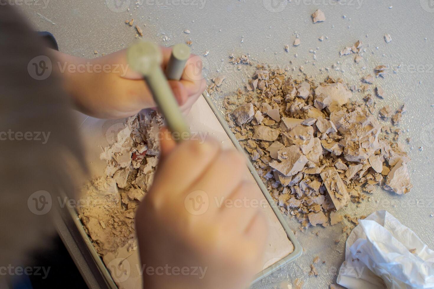 Top view of a child with the help of a geologist's kit extracts a jasper in a plaster cast photo