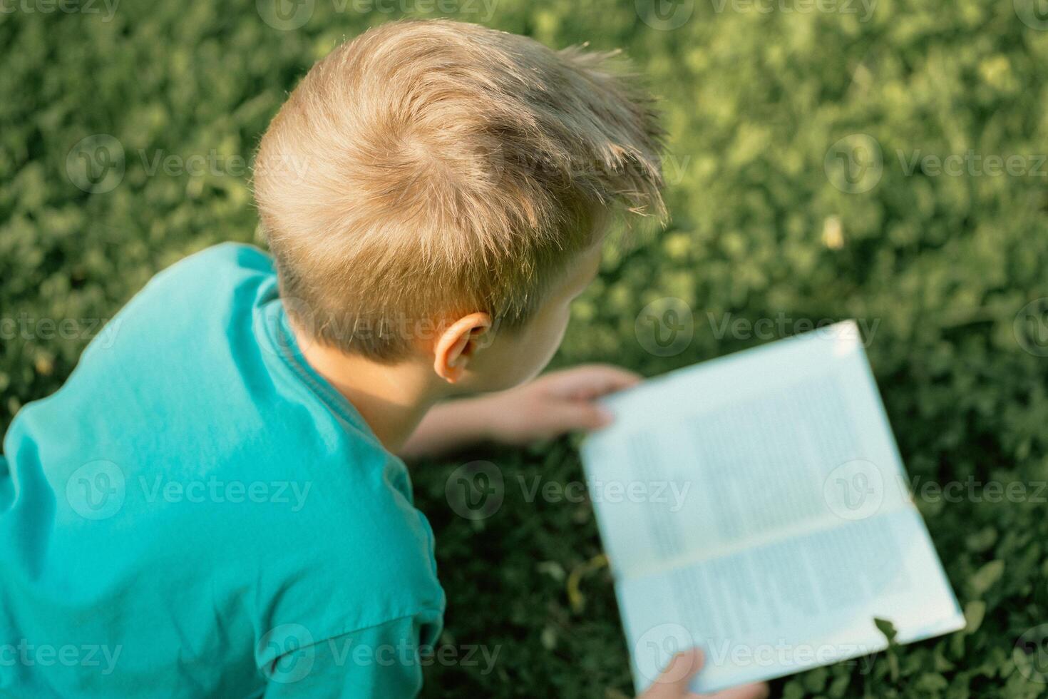 A boy in a blue T-shirt reads a book in a park on the grass photo