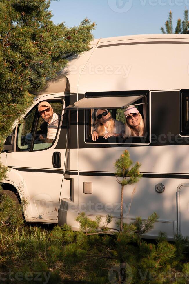 Family enjoying a sunny day in a camper van surrounded by tall trees in a peaceful countryside setting during summer photo