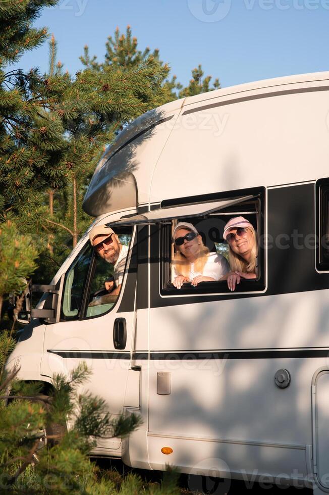 Family enjoying a sunny day in a camper van surrounded by tall trees in a peaceful countryside setting during summer photo