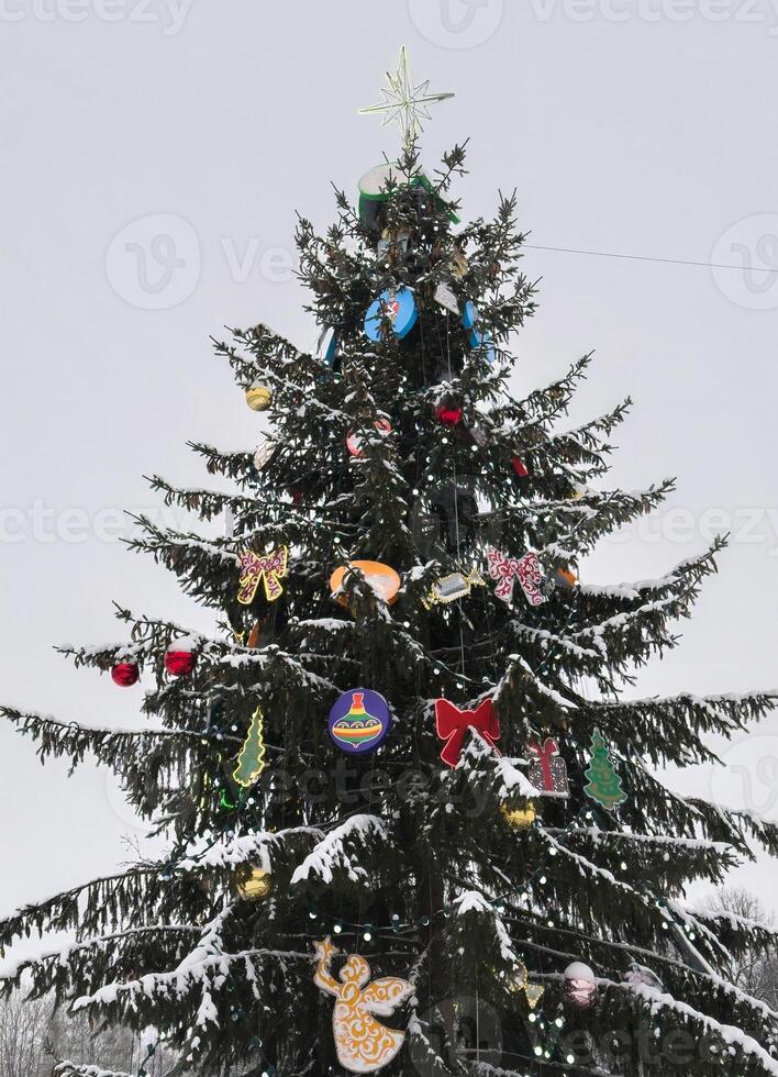 A beautifully decorated Christmas tree covered in fresh snow stands against a winter sky. Colorful ornaments, glowing lights, and a shining star at the top create a festive holiday atmosphere photo
