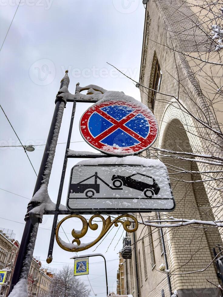 Traffic signs covered in fresh snow stand against the backdrop of a winter cityscape. The speed limit and road signs are partially obscured, blending into the frosty urban environment photo