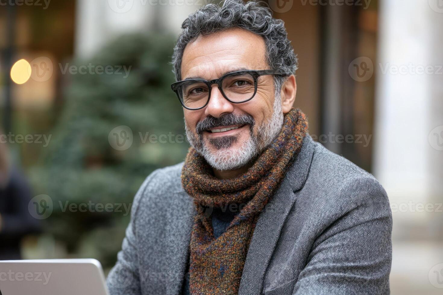 Smiling man with laptop wearing scarf enjoys outdoor workspace in urban setting during day photo