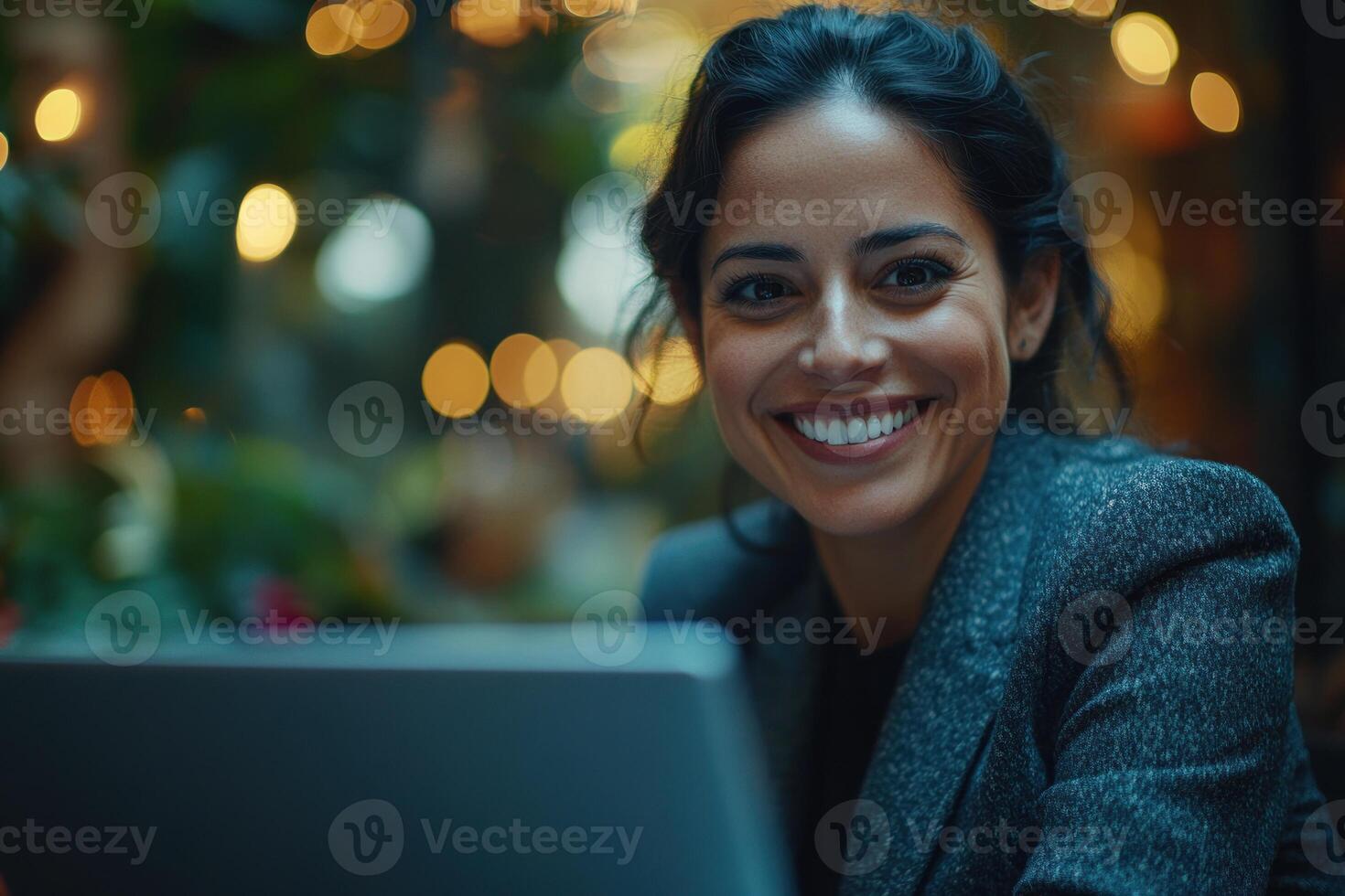 Smiling woman working on a laptop in a cozy, illuminated cafe during evening hours photo