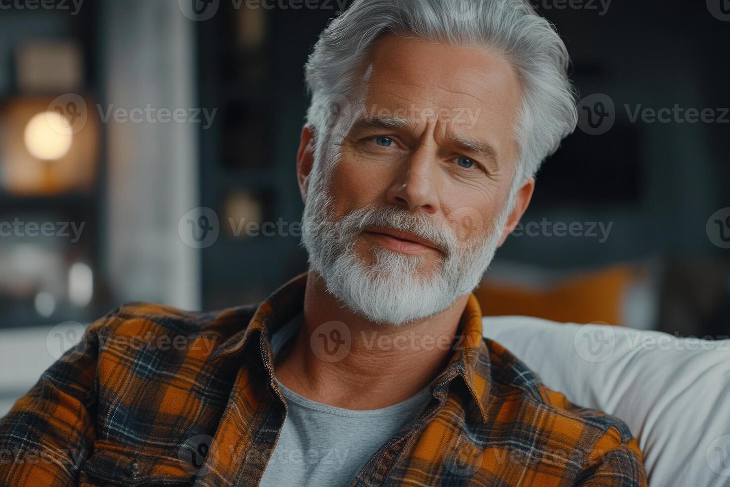 Older man with gray hair and beard relaxes on a couch at home during the evening photo