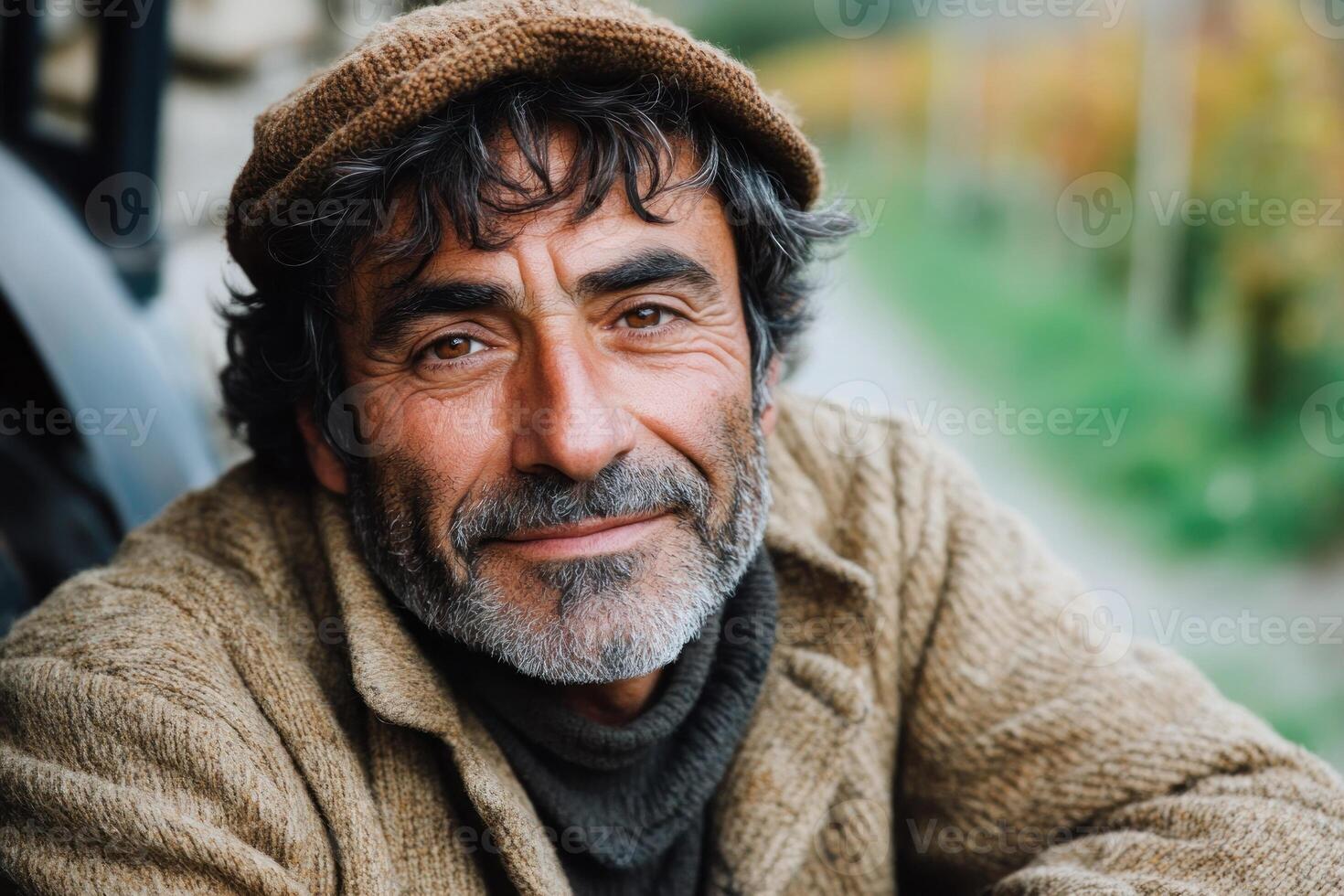Smiling man with gray beard and warm sweater poses outdoors in a vineyard during the day photo