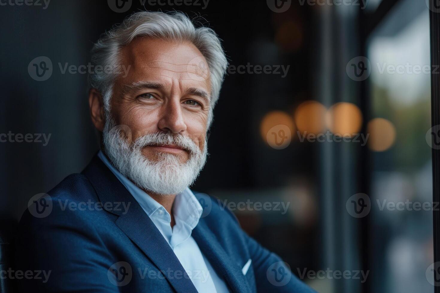 Senior man with silver hair and beard smiles warmly, showcasing professionalism in a modern setting photo