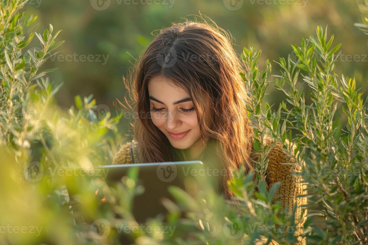 Young woman enjoys reading on tablet surrounded by lush greenery in outdoor setting photo