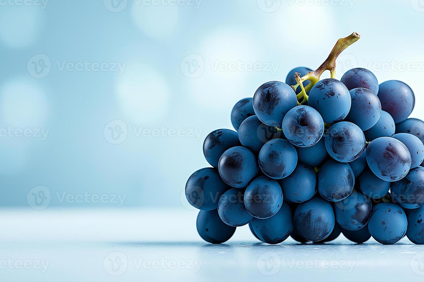 Fresh blue grapes stacked on light blue background, creating vibrant and appealing display. soft focus adds dreamy quality to image, enhancing its visual charm photo