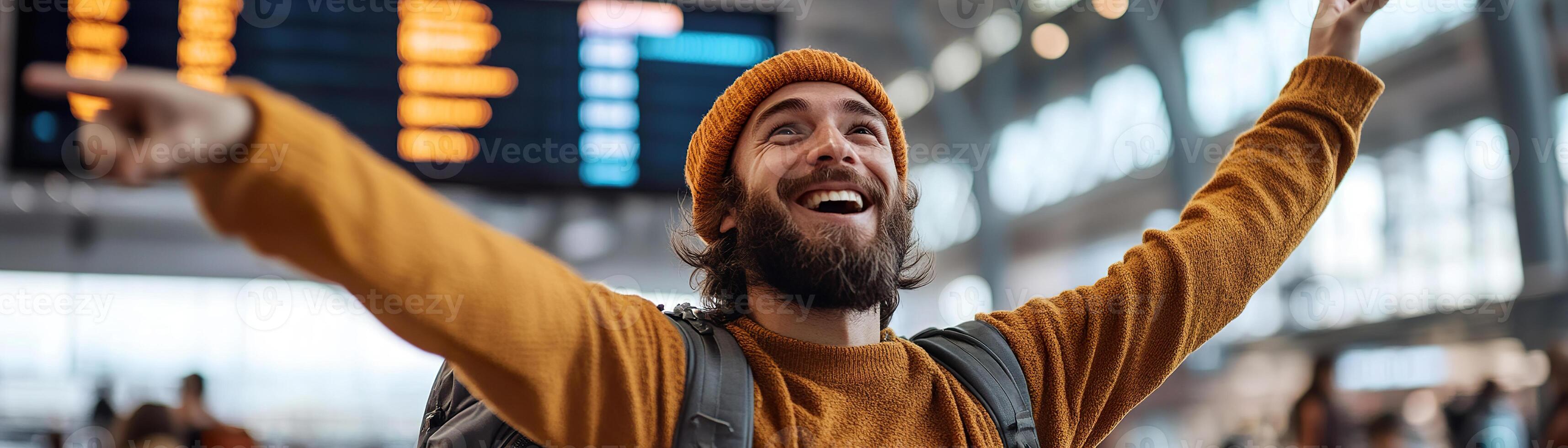A joyful traveler stands in an airport terminal, pointing towards a digital departure board. The bustling background highlights the vibrant energy of travel, capturing a moment of excitement photo