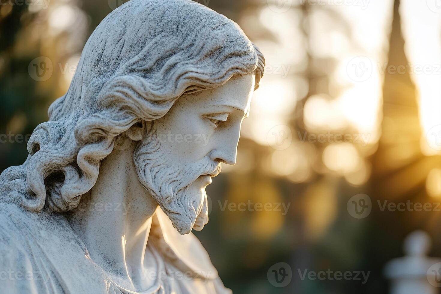 A beautifully sculpted statue of Jesus receives divine light. Soft-focus sunlight filters through trees. A warm glow highlights his serene expression photo