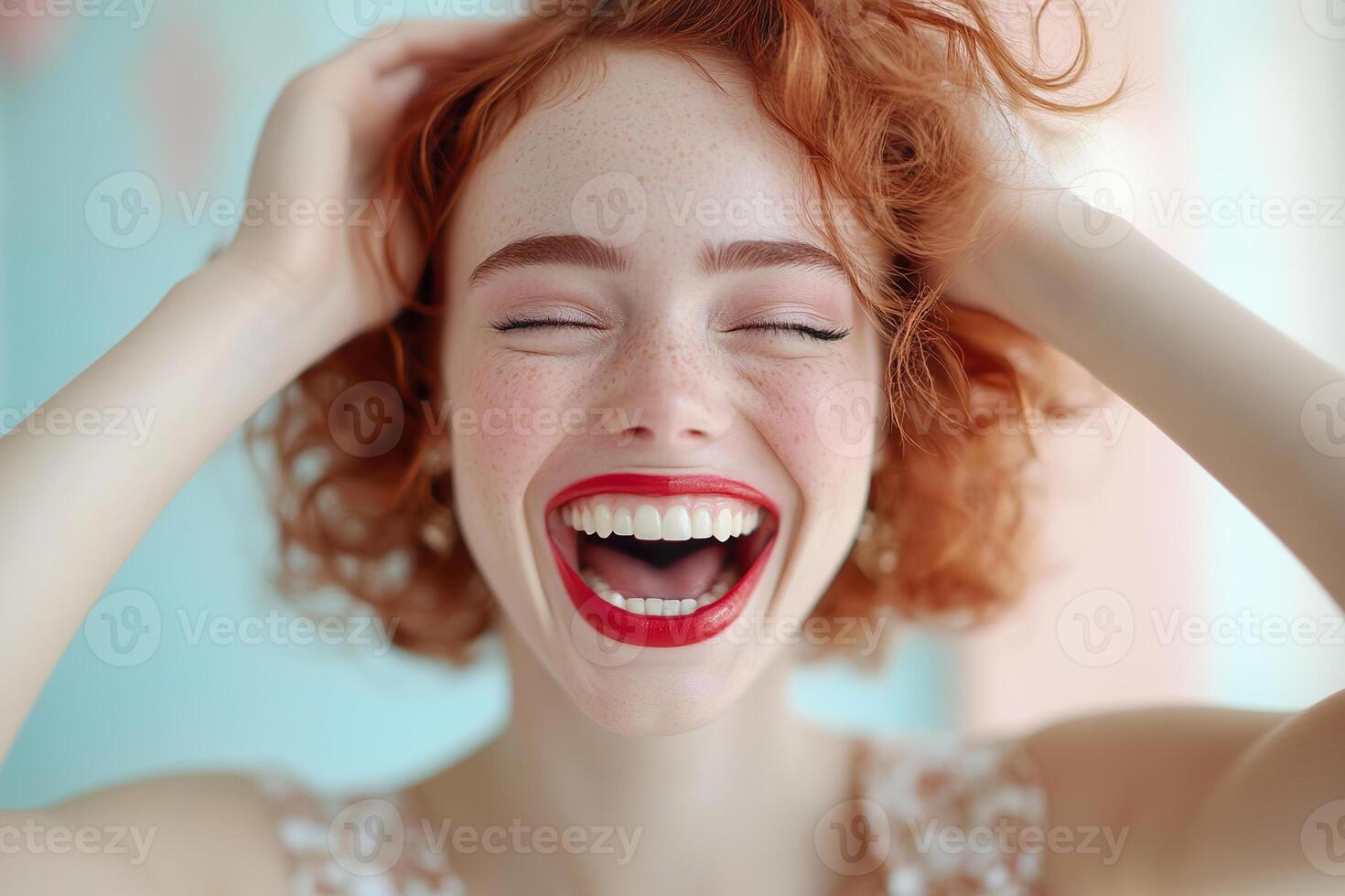 A woman with curly red hair and bold red lipstick laughs joyfully, with her hands playfully touching her hair. Soft pastel colors create a glamorous and cheerful background photo