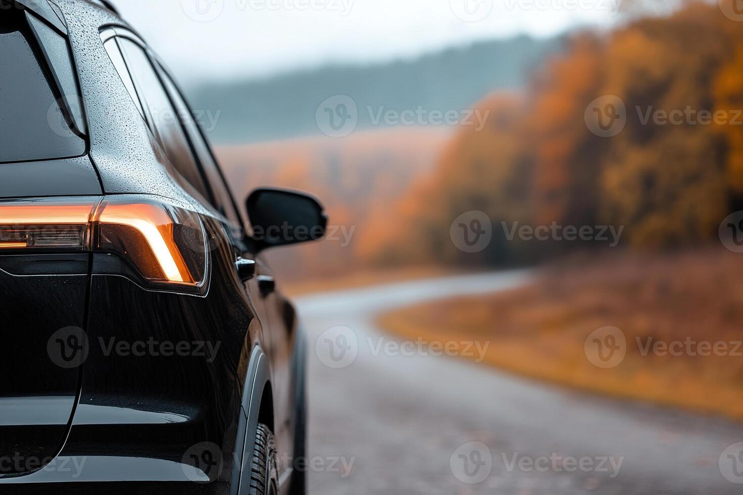 A black SUV is parked beside a winding road, with raindrops on its surface. Colorful autumn leaves surround the area, creating a serene and picturesque atmosphere photo