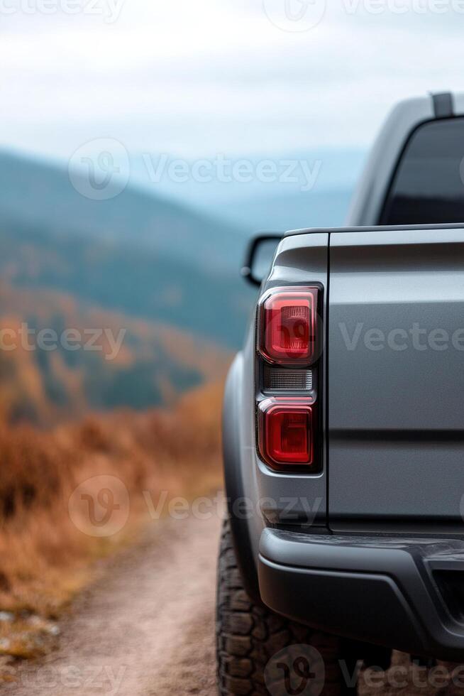 A gray truck is parked along a winding dirt road, framed by rolling mountains and rich autumn leaves. The atmosphere is calm with overcast skies, creating a serene outdoor setting photo