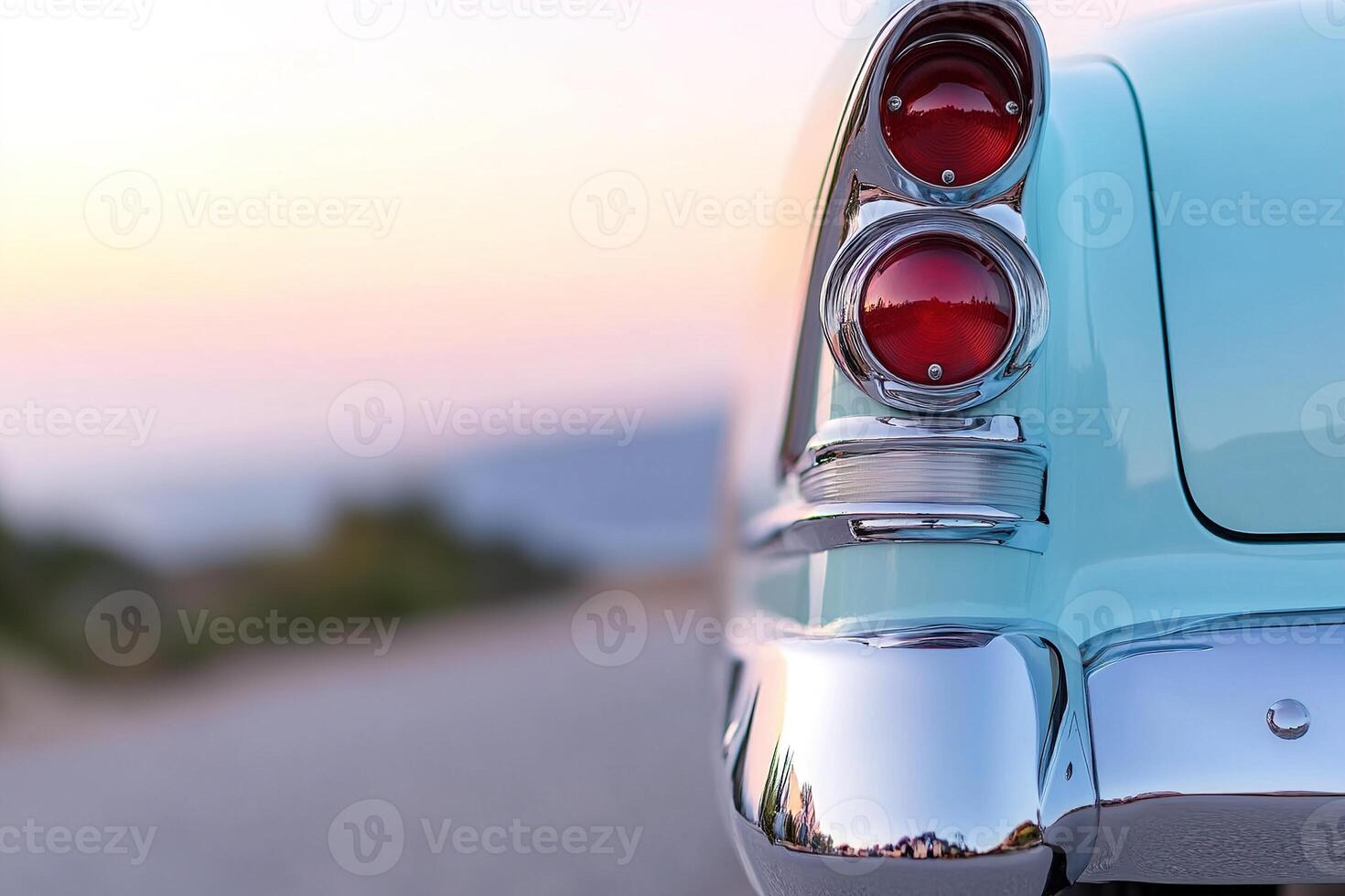 A vintage car, painted in light blue, displays its gleaming tail lights while parked on a scenic coastal road at sunset, showcasing the serene atmosphere and natural colors photo