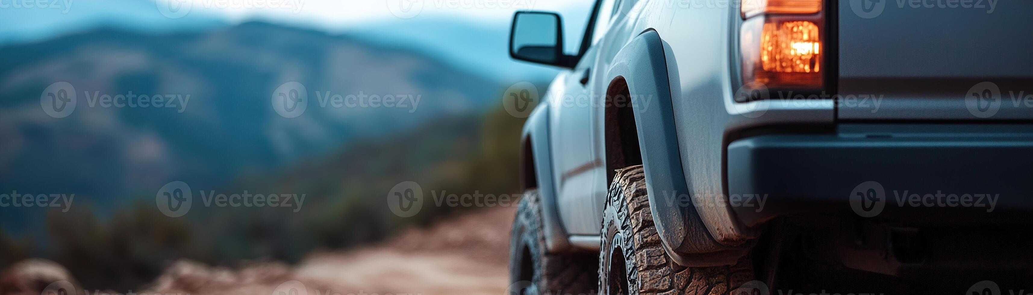A rugged vehicle navigates a mountainous terrain, its tires gripping the rocky path as the sun sets behind distant peaks, casting warm hues across the landscape photo
