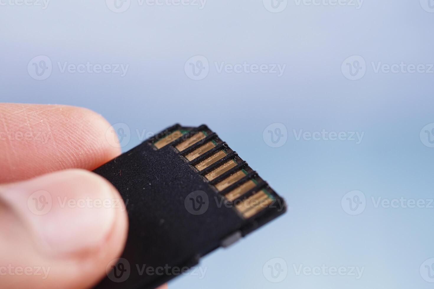 Hand holding a micro SD card with a blurred background photo