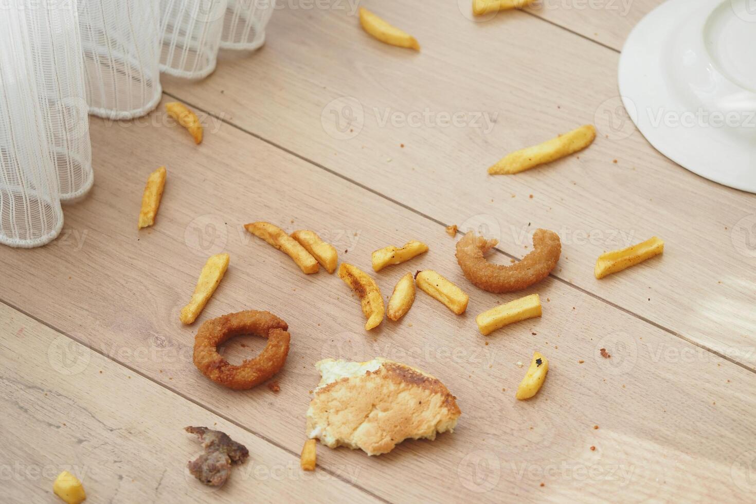 Food scraps scattered on a wooden floor near a curtained window photo