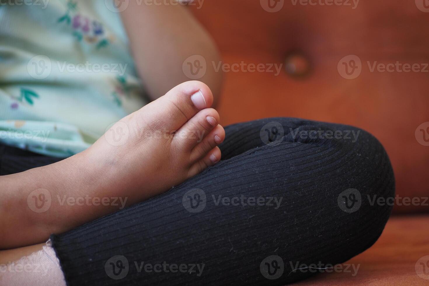 Child resting feet on knee while sitting comfortably indoors photo
