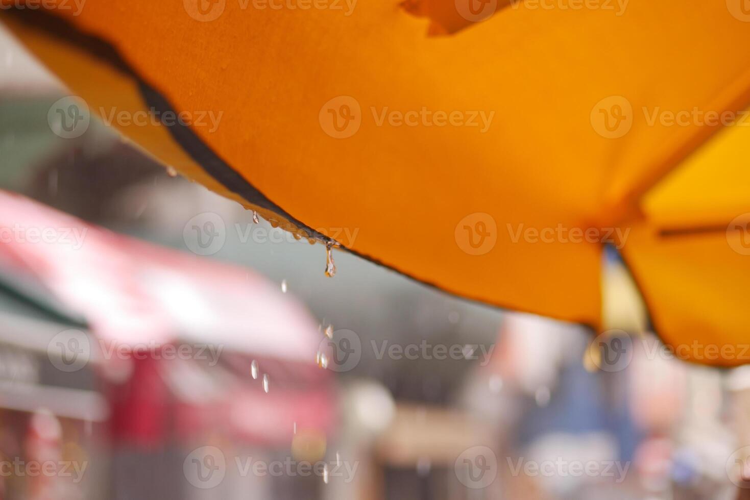 Rain falling from a yellow umbrella on a busy street photo