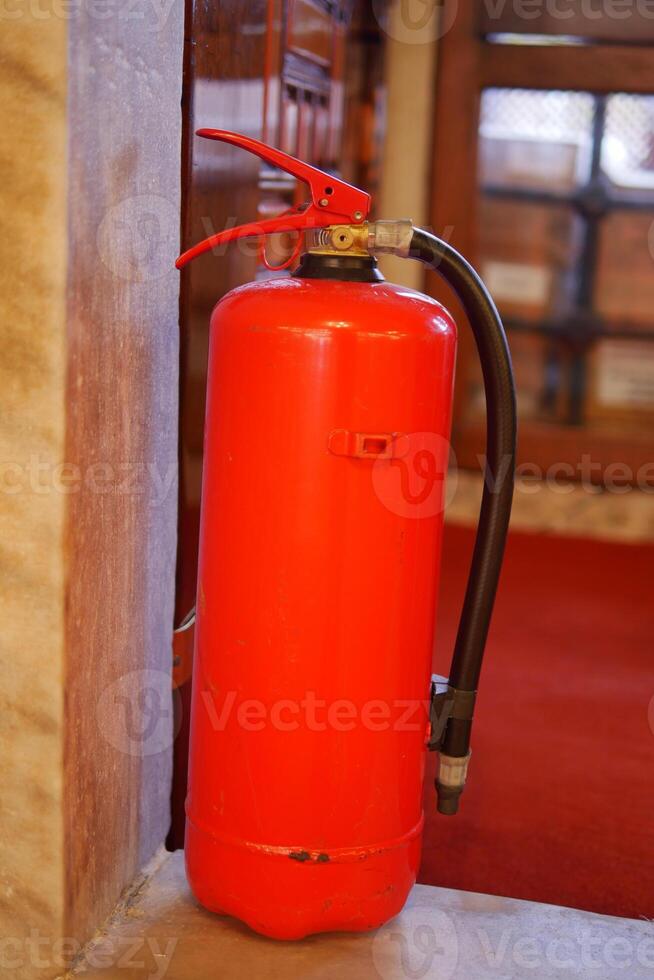 Fire extinguisher positioned beside a wall in an indoor setting photo
