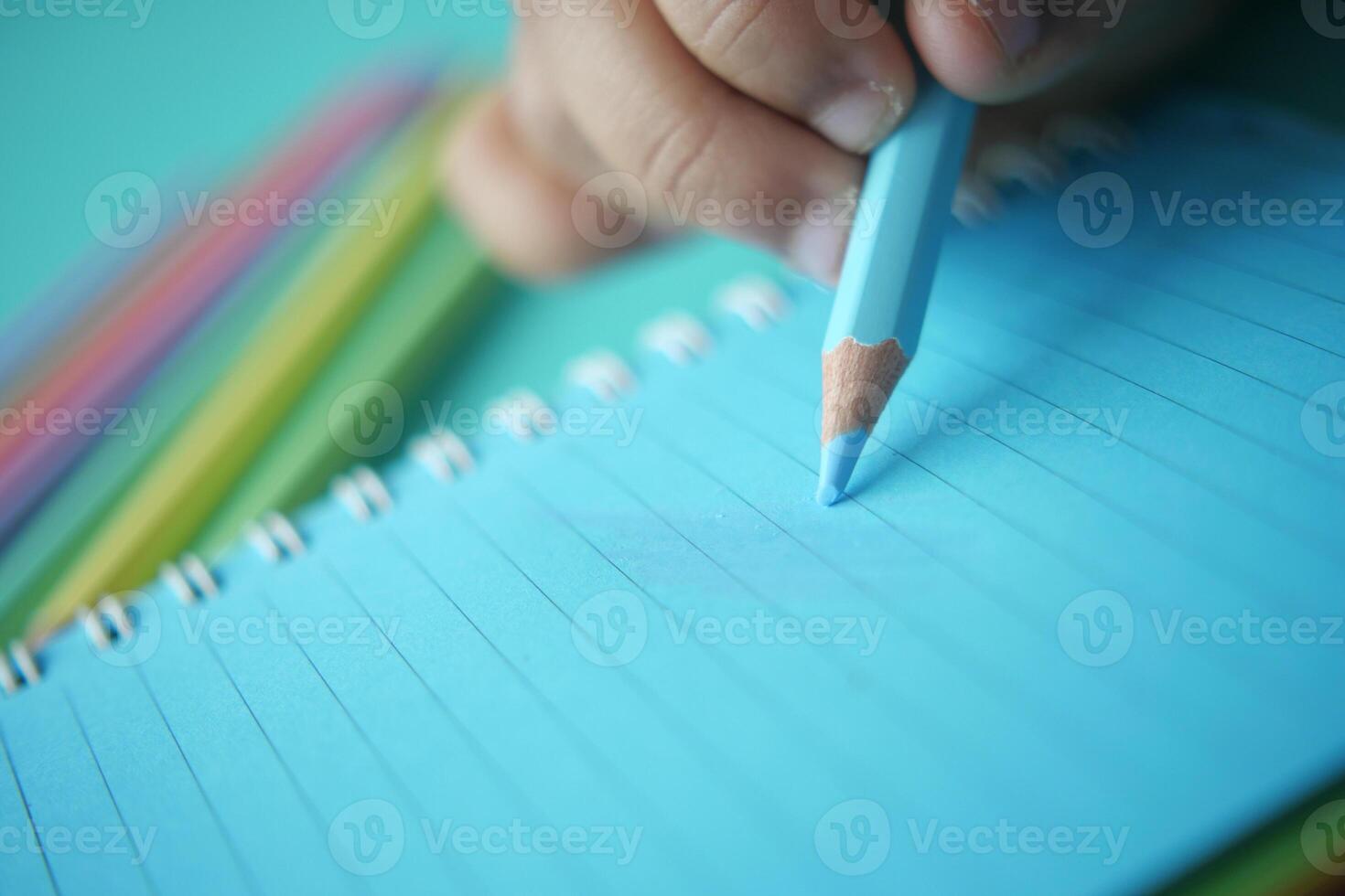 Child drawing with colored pencil in a spiral notebook photo
