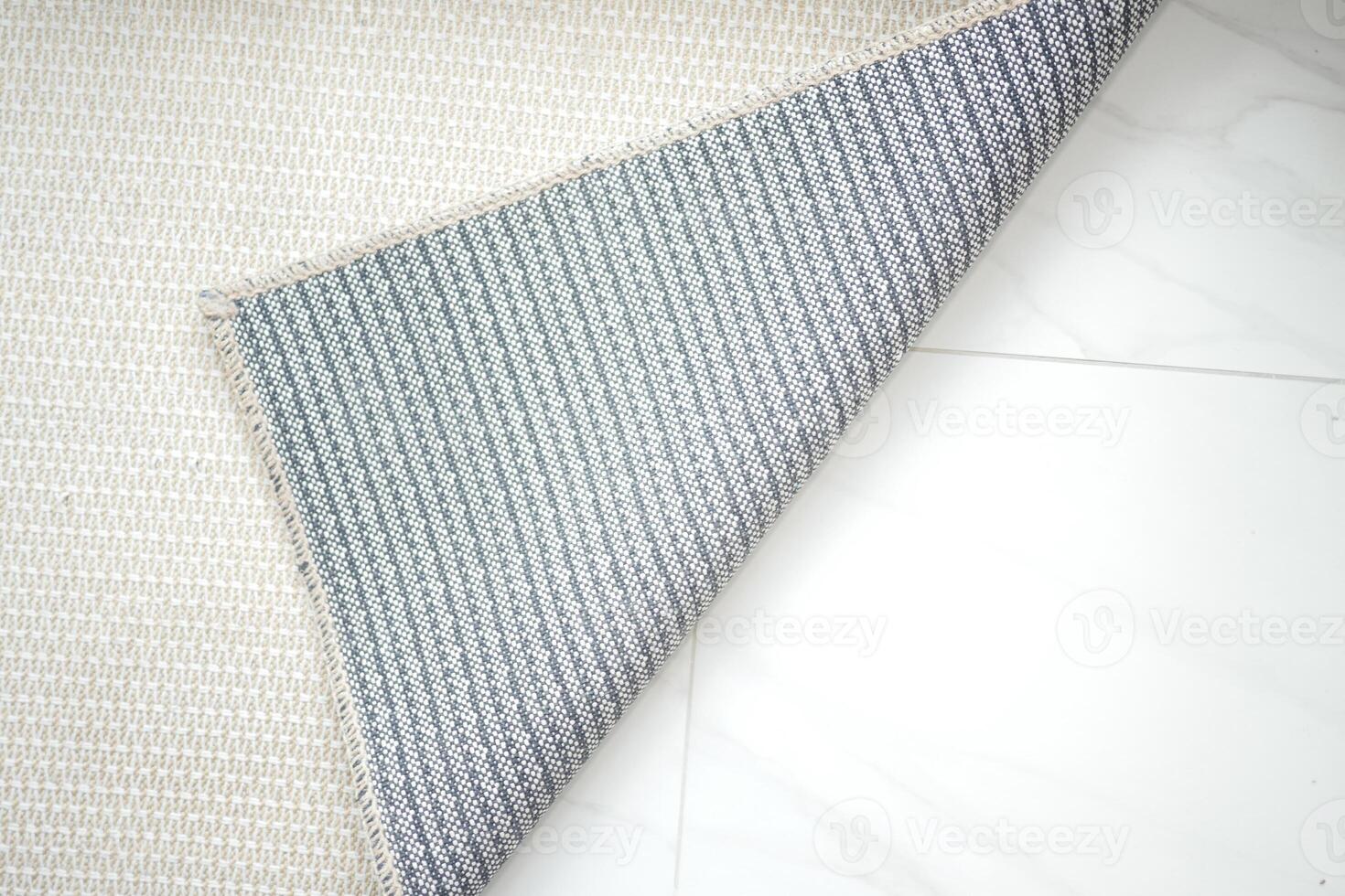 Elegant rug with gray pattern partially rolled on white tiles photo