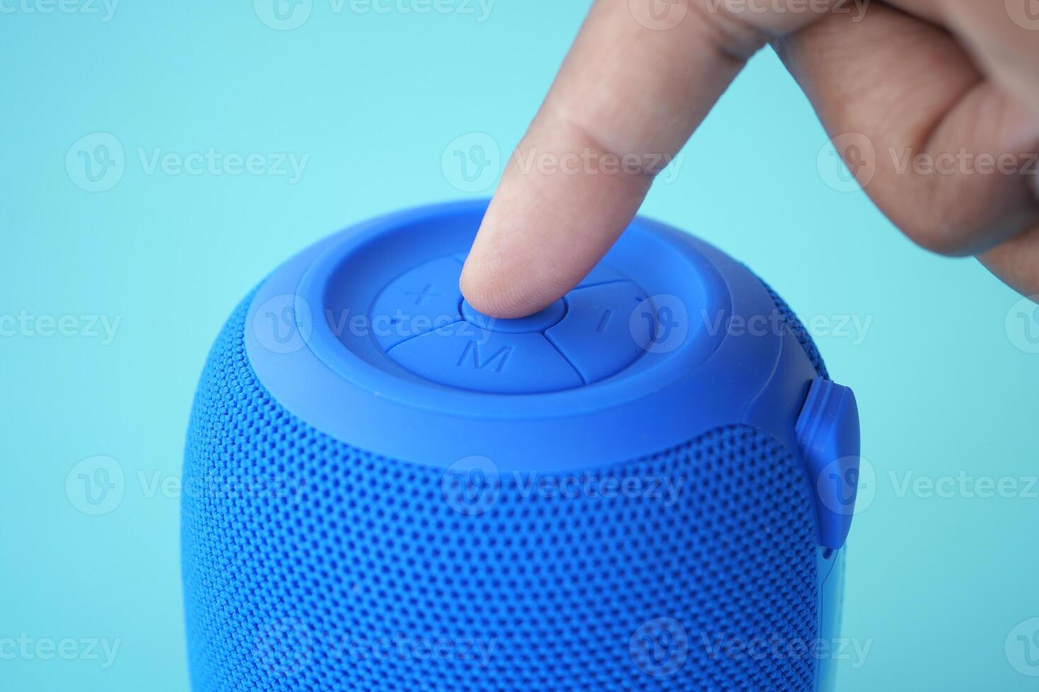 Close-up of a hand pressing a button on a portable blue speaker photo