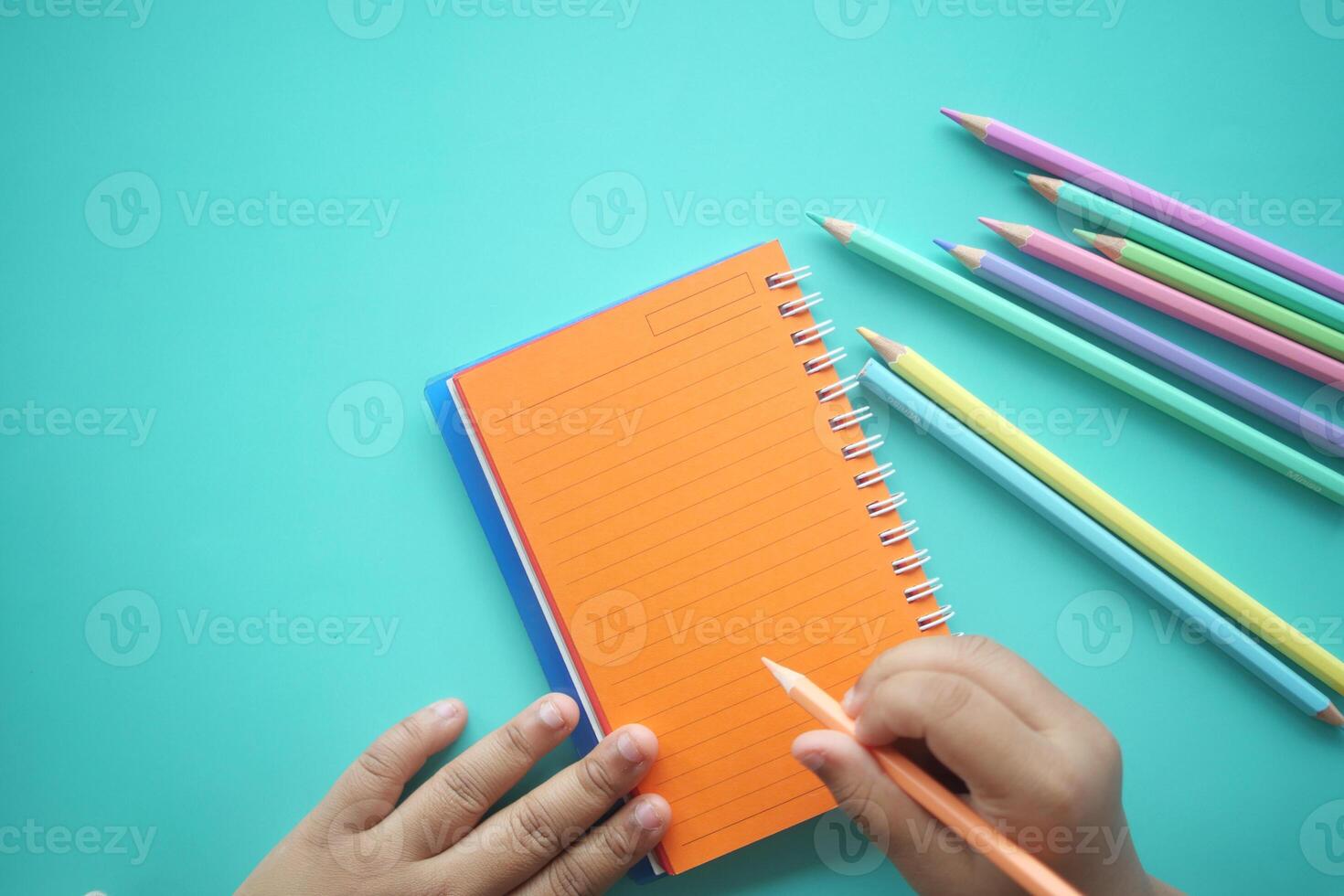 Child writing in a notebook with colorful pencils on a table photo